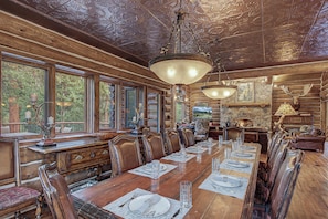 A log cabin interior with a long dining table set for six, wooden walls, and a stone fireplace. - Luxury w/ River Views + Hot Tub + Private Shuttle - Rivertree Lodge (Breckenridge)