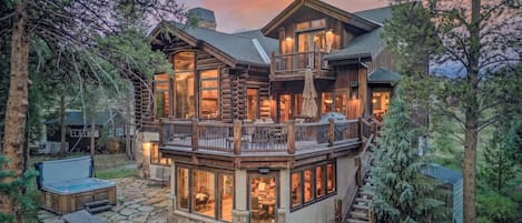 A large log cabin with multiple levels, outdoor seating, and a hot tub.