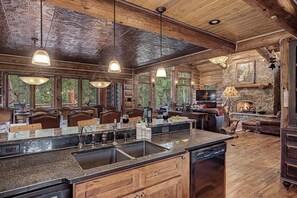 A spacious kitchen with a large island, wooden cabinetry, and a stone fireplace. - Luxury w/ River Views + Hot Tub + Private Shuttle - Rivertree Lodge (Breckenridge)