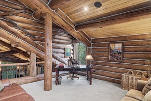 A log cabin interior with a wooden ceiling, a table with books and a moose statue, and a view of trees through a window. - Luxury w/ River Views + Hot Tub + Private Shuttle - Rivertree Lodge (Breckenridge)