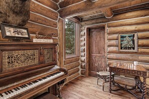 Ein Holzblockhaus-Interieur mit einem Klavier, einem Schachbrett und einer Tür, die nach draußen führt.