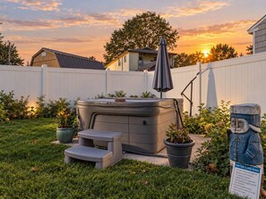 Un bain à remous dans un jardin, avec une clôture blanche, des plantes en pot et une sculpture en bois.