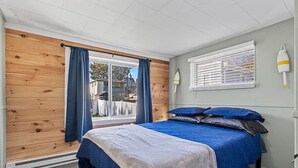 Et soveværelse med seng, et vindue med gardiner, en vægmonteret lampe og udsigt ud