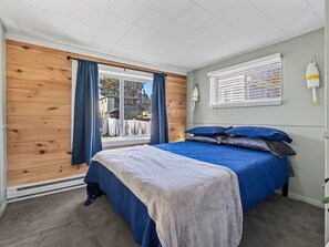 Un dormitorio con una cama, una ventana con cortinas, una lámpara fijada a la pared y vistas al exterior.