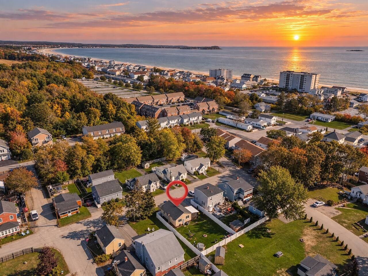 Oversigtsbillede af et boligområde med huse, en strand og en solnedgang.
