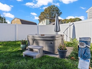 Un patio trasero con un jacuzzi, una banca, plantas en macetas y una escultura de madera.