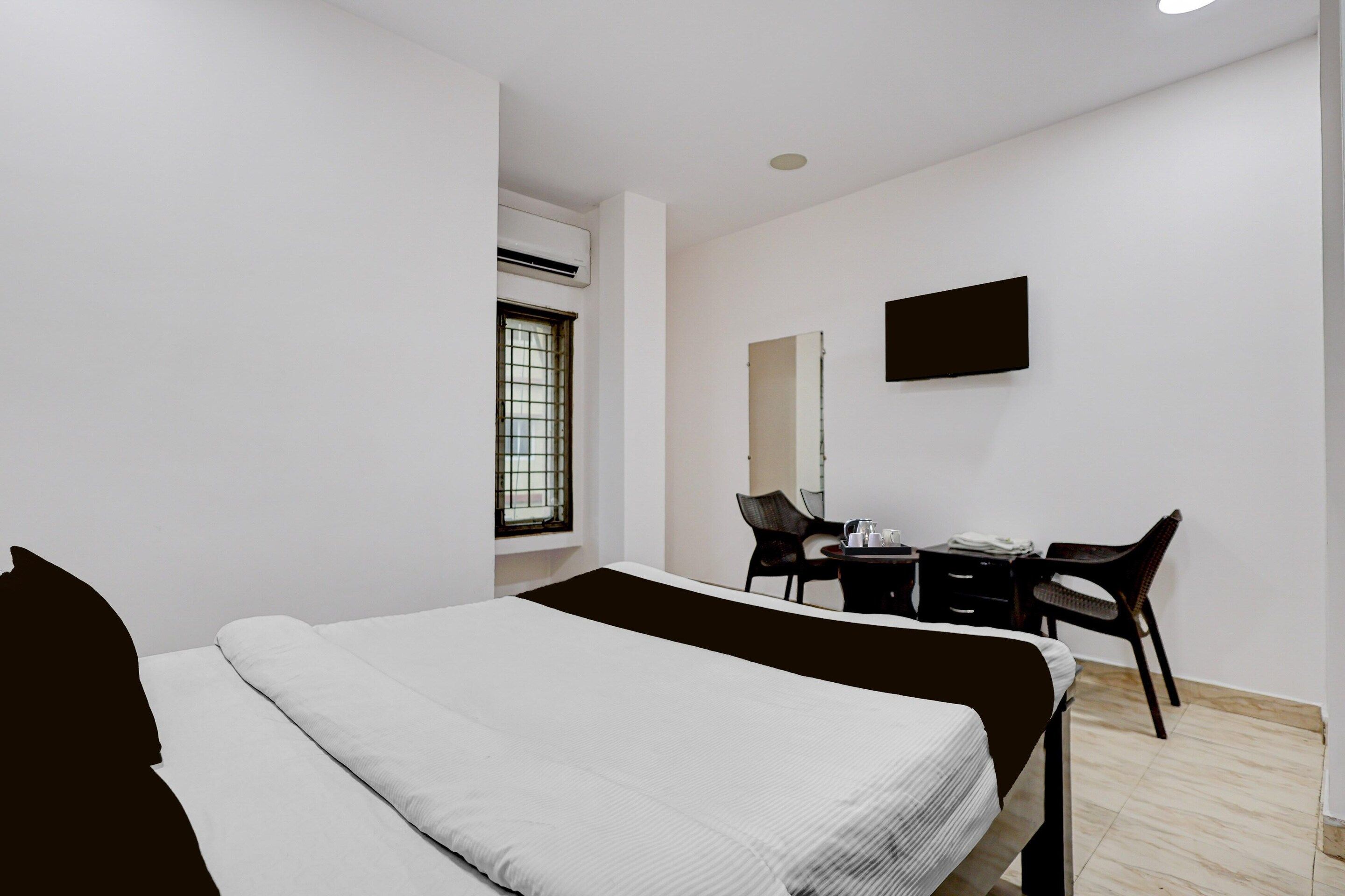 A hotel room with a bed, a desk, a chair, and a TV mounted on the wall.