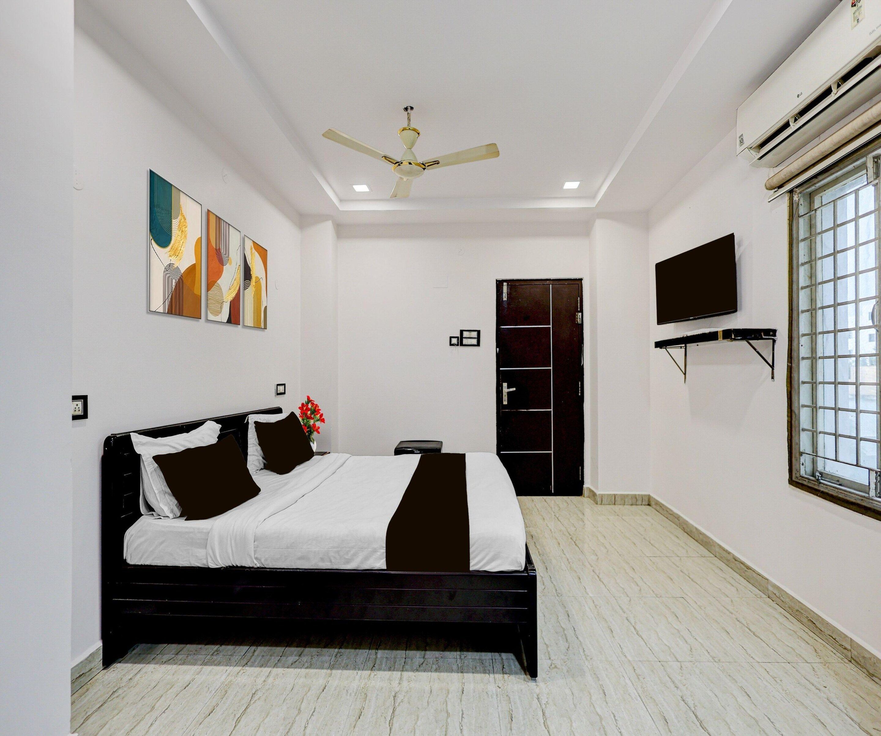 Ein Hotelzimmer mit einem Bett, Deckenventilator, Kunstwerken, Fernseher und einem Fenster.