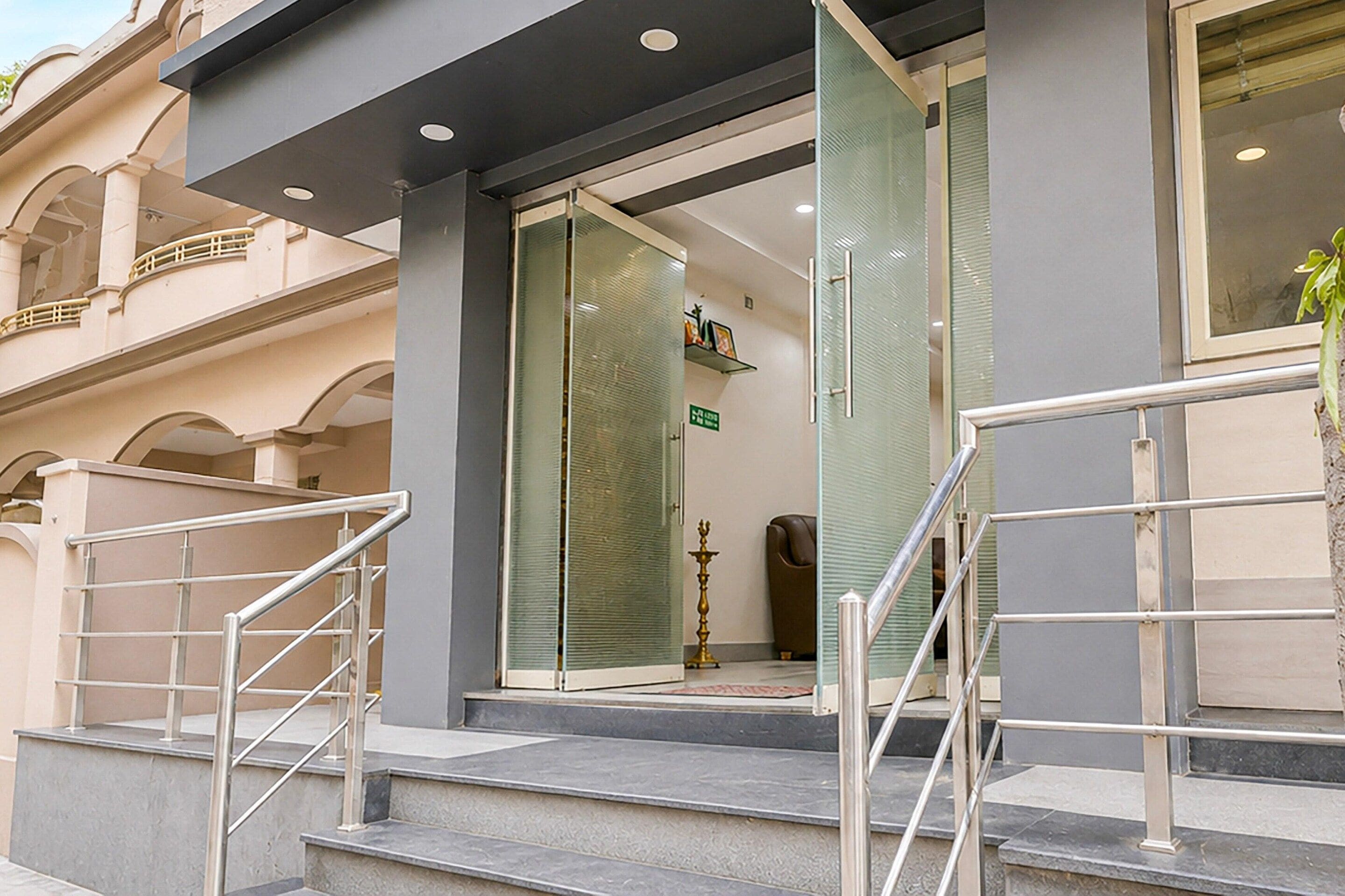 A hotel entrance with a glass door, a staircase with metal railings, and a small plant on the right.