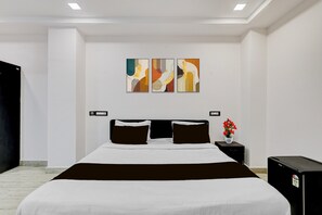 A hotel room with a large bed, a nightstand with a vase of flowers, and three abstract paintings on the wall.