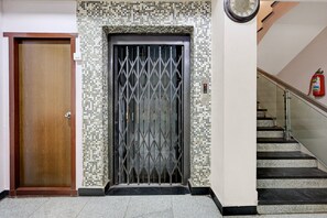 Una puerta de madera, un portón metálico con un diseño de rombos y una escalera con un extintor en la pared.