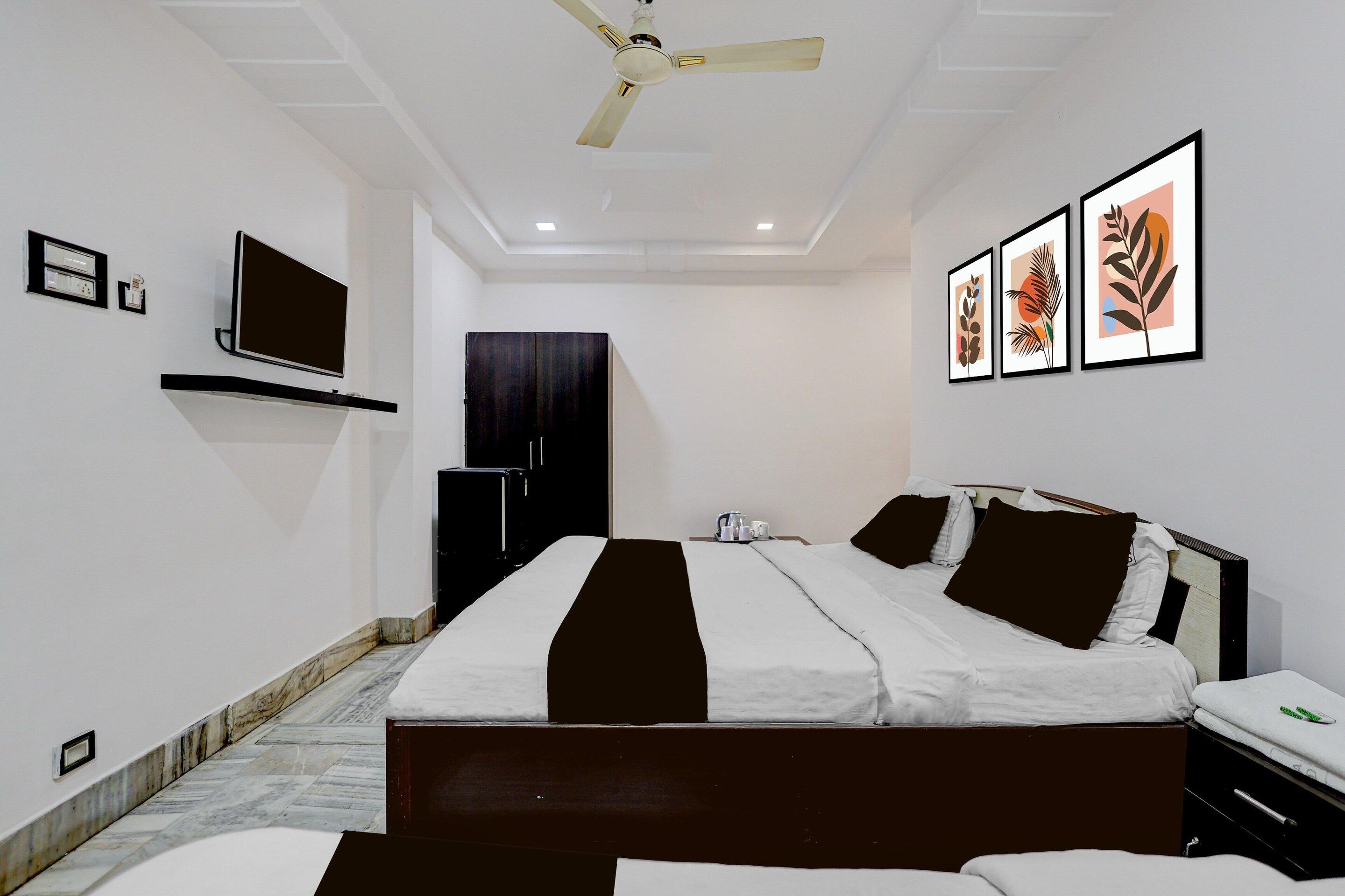 A hotel room with a bed, a television, artwork on the wall, and a ceiling fan.