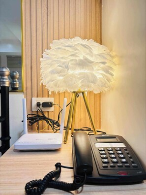Ein Schreibtisch mit einem weißen Laptop, einem schwarzen Telefon und einer dekorativen Lampe mit Federlampe.