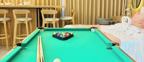 A pool table with a cue stick, a billiard ball, and a set of pool balls in the center.