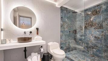 Un baño moderno con un espejo redondo, un lavabo blanco y una ducha con cerramiento de vidrio.