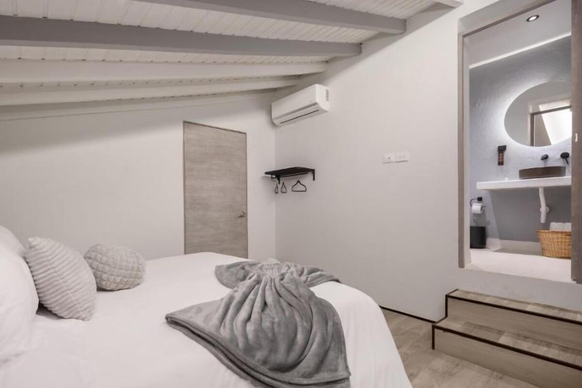 Un dormitorio con cama, almohadas, una manta, un espejo y una puerta.
