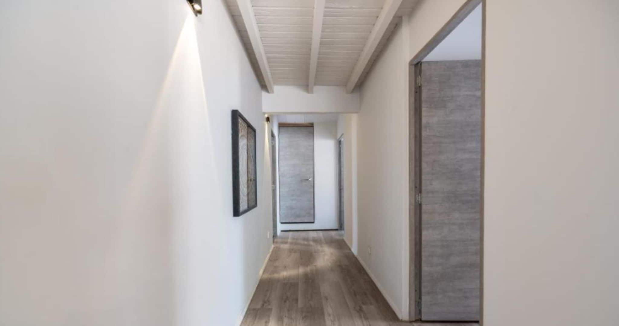 Un pasillo con piso de madera, paredes blancas y una puerta al final.