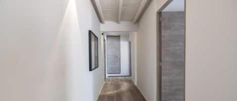 A hallway with a wooden floor, white walls, and a door at the end.