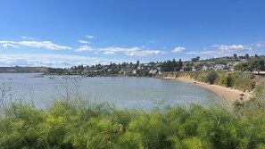 A coastal landscape with a sandy beach, a calm lake, and residential buildings in the background.