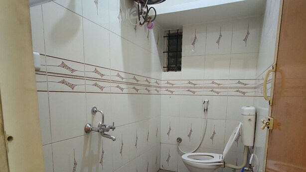 Een compacte badkamer met toilet, douche en boiler. Op de vloer staat een prullenbak en een blauwe bak.