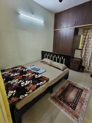 Quarto com cama, mesa de cabeceira, guarda-roupa, espelho e tapete estampado.