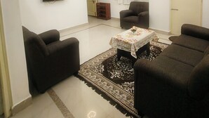 Een woonkamer met een flatscreen televisie, plafondventilator en een kamerkleed met dessin.