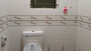 Een kleine badkamer met tegels, een toilet, een raam en een douchehoek.