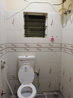 Um banheiro pequeno revestido com azulejos, com vaso sanitário, janela e área de chuveiro.