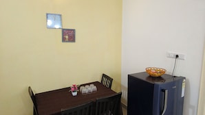 Een eetruimte met een tafel, stoelen, een koelkast en wandlampen.