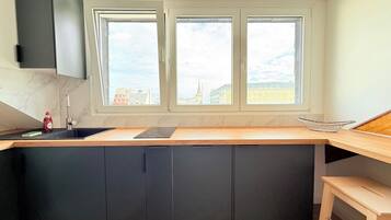 Cozinha moderna com ilha central, armários escuros, janela com vista para a cidade e lava-louças embutida.
