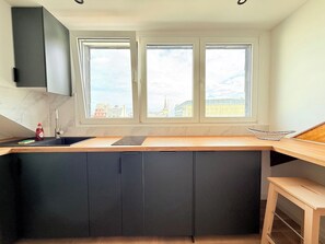 A modern kitchen with a central island, dark cabinets, a window with a city view, and a built-in dishwasher.