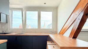 Cozinha moderna com mesa de jantar de madeira, dois banquetes e vista para a cidade através de grandes janelas.