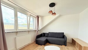 Uma sala de estar moderna com sofá seccional, uma mesa de centro branca e vista para o exterior através de grandes janelas.