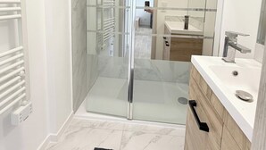 Um banheiro moderno com chuveiro envidraçado, toucador branco com pia e espelho.