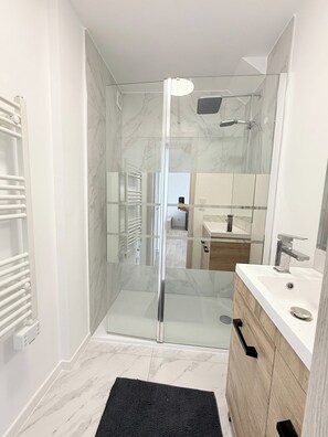 Un baño moderno con ducha de vidrio, tocador blanco con lavamanos y espejo.