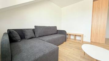 Uma sala de estar moderna com um sofá seccional cinza, uma mesa pequena branca e uma porta de madeira.