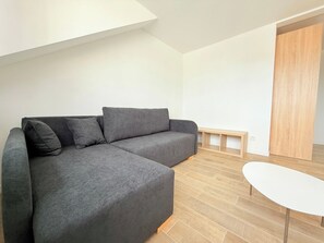 A modern living room with a grey sectional sofa, a small white table, and a wooden door.