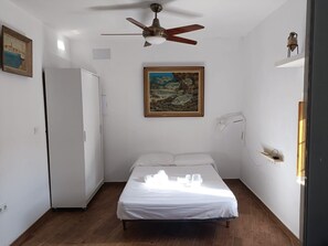 A bedroom with a bed, a ceiling fan, a painting, a white wardrobe, and a small shelf. - El Porky del Almirante, a little cottage near the sea. Enjoy it with your pet. (Las negras)