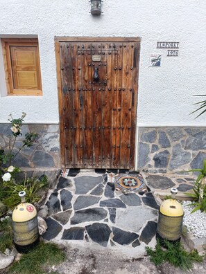 A wooden door with a metal latch, a stone-paved entrance, and a sign above the door. - El Porky del Almirante, a little cottage near the sea. Enjoy it with your pet. (Las negras)