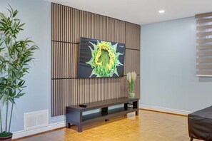 Un salon moderne doté d’un grand téléviseur fixé au mur, d’un mur décoré de lambris en bois, d’une console sombre et d’une plante en pot.