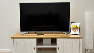 Een flatscreen televisie op een houten tv-meubel, met een afstandsbediening, een lijst met een foto en een lamp.