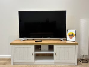 A flat-screen TV on a wooden TV stand with a remote control, a framed picture, and a lamp. - Tantin Suite: 61 m² Loft in Downtown Santander, High Ceilings. (Santander)