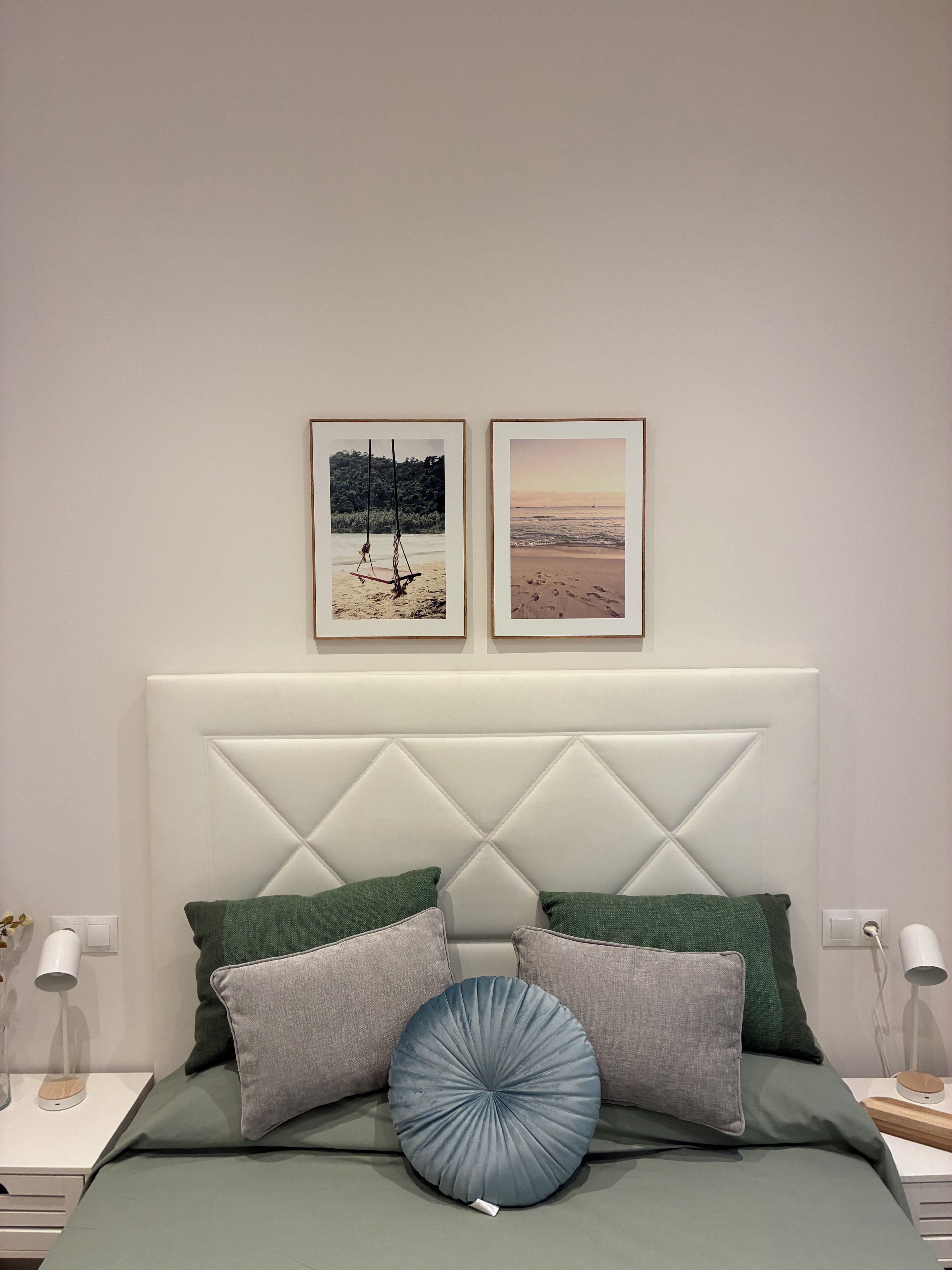 Une chambre à coucher avec un lit, des oreillers, une tête de lit et deux tableaux encadrés accrochés au mur.