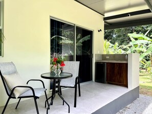Un patio con dos sillas, una mesa, una puerta corrediza de vidrio y una pequeña cocina.