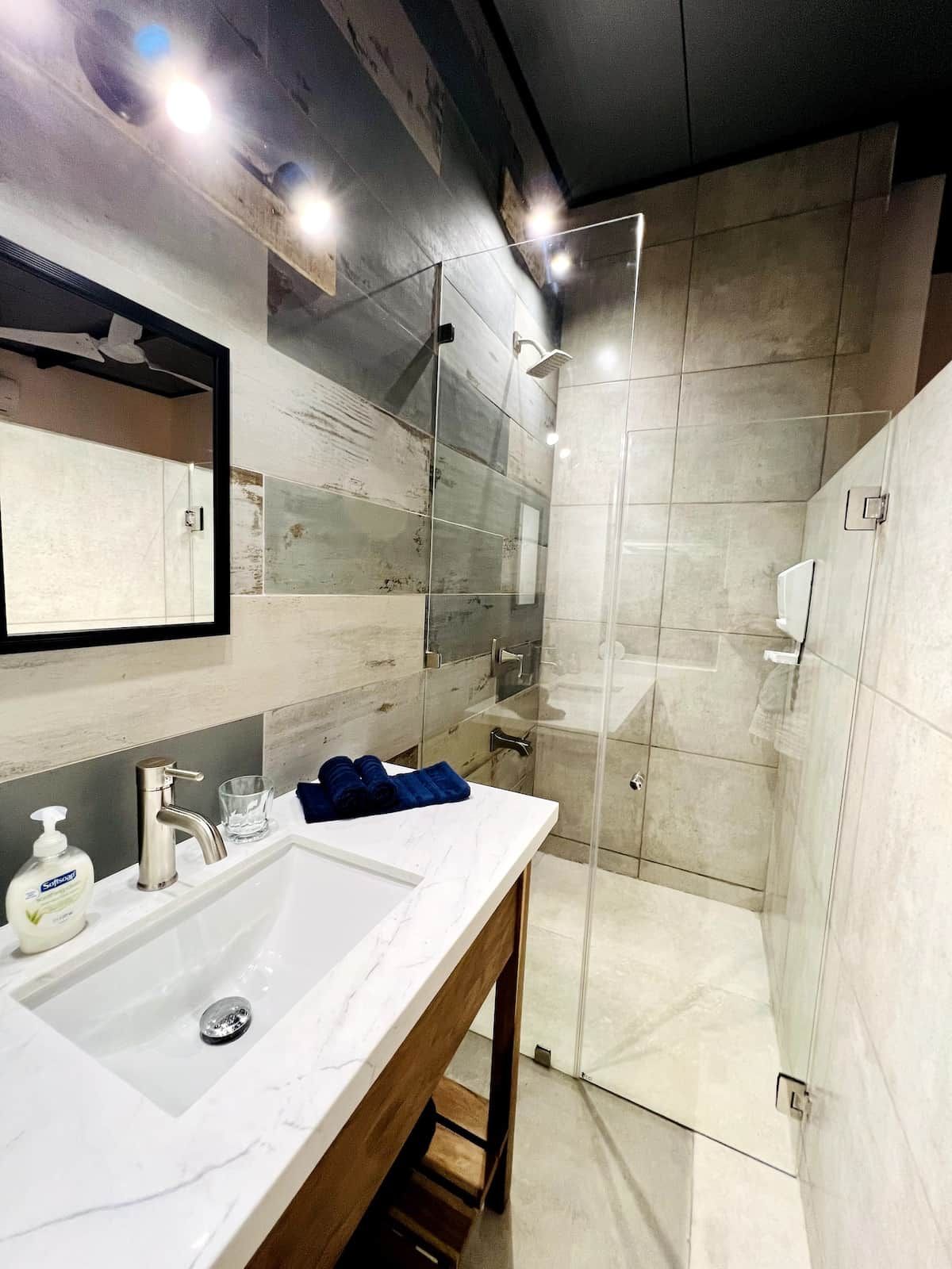 Une salle de bain moderne avec une douche à parois de verre, un lavabo en marbre et un miroir.