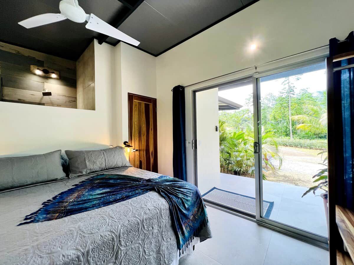Een slaapkamer met een bed, een plafondventilator, een houten deur en een schuifdeur van glas die uitkomt op een tuin.