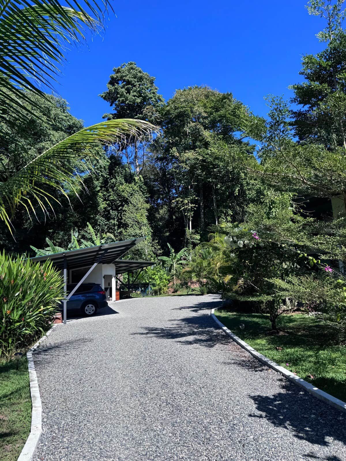 A gravel driveway leading to a covered car parking area with a building in the background.