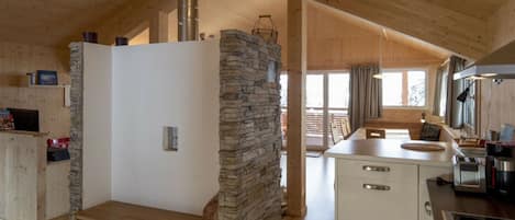 Un interior de madera con pared de piedra, banco de madera, kitchenette y vistas a través de un vano.