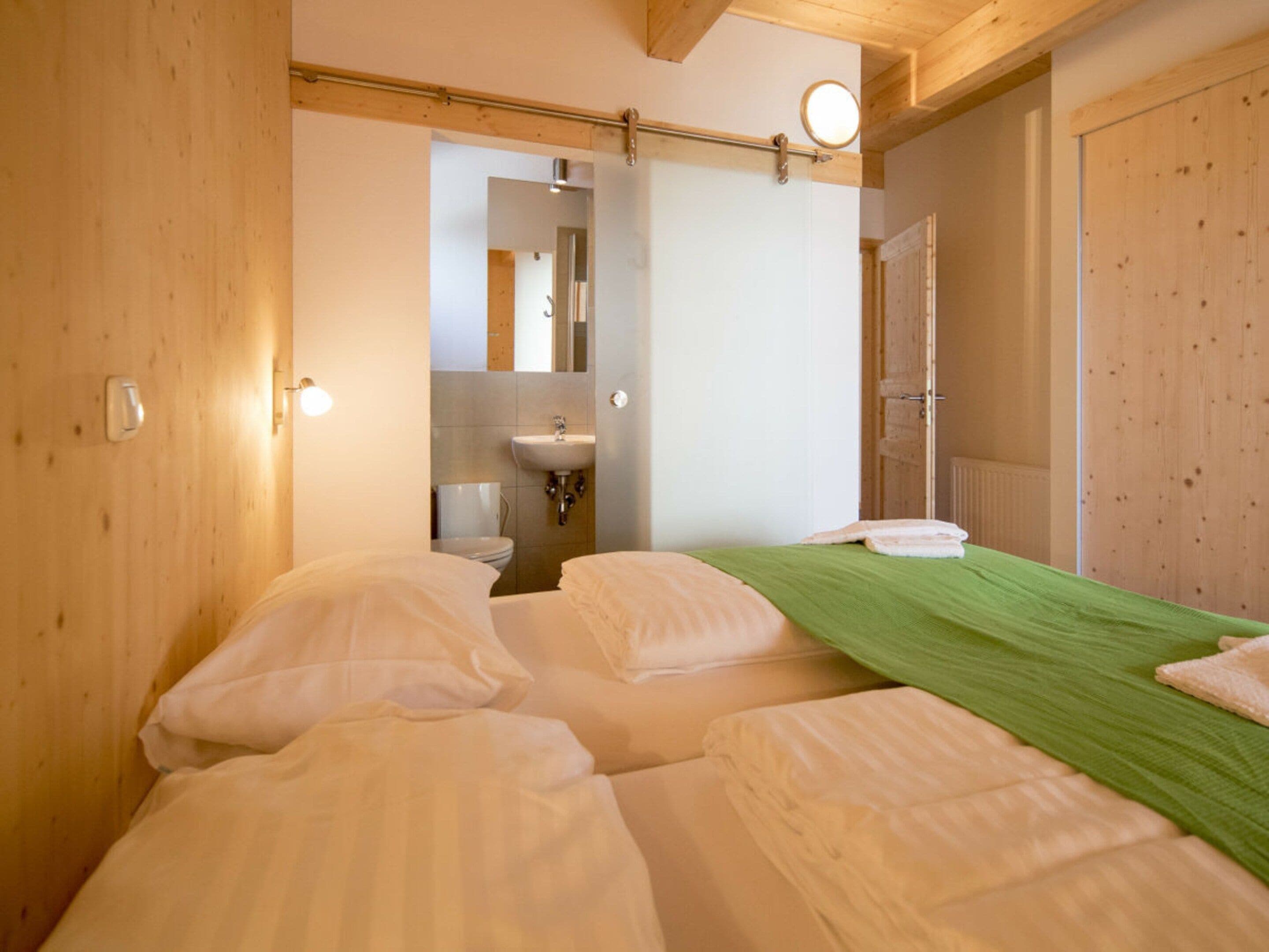A hotel room with two beds, a bathroom with a sink, and wooden walls.