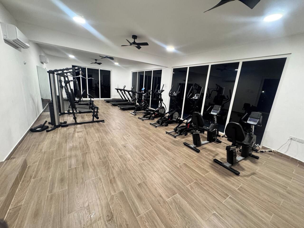 A gym with various exercise equipment, large windows, and a wooden floor.